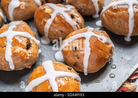 Petits pains croisés chauds faits maison fraîchement glacés et sur une plaque à biscuits. Banque D'Images