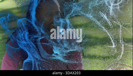 Homme assis avec des dreads en veste rouge souriant sur l'herbe du parc, hologramme bleu, panier et enfant Banque D'Images