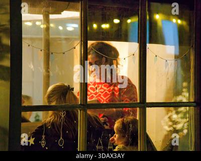 Un aperçu à travers une fenêtre festive et décorée d'une serveuse prenant une commande familiale dans un restaurant à Noël. Prise à Bourton sur l'eau. Banque D'Images