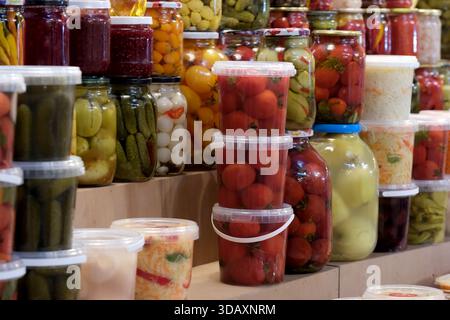 Des pots lumineux remplis de légumes marinés sont empilés dans une scène de marché animée. Kiev, Ukraine. 12 décembre 2025. Banque D'Images