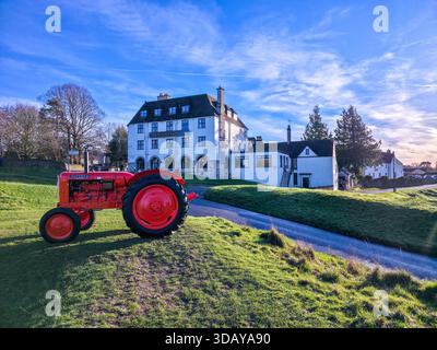 Tracteur vintage rouge à Golden Hour devant Cotswolds Manor House Banque D'Images