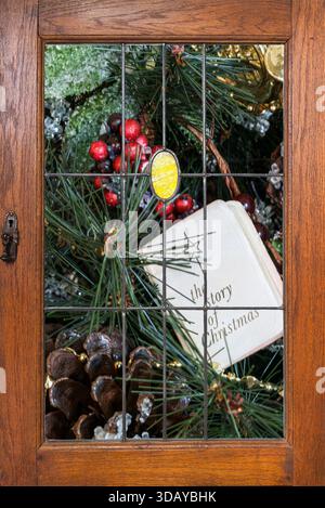 Dans le cabinet derrière le verre de fenêtre voir les ornements de Noël, Bible, verdure. Le livre blanc a l'histoire de Noël de la Bible. Voir baies rouges et pommes de pin. Banque D'Images
