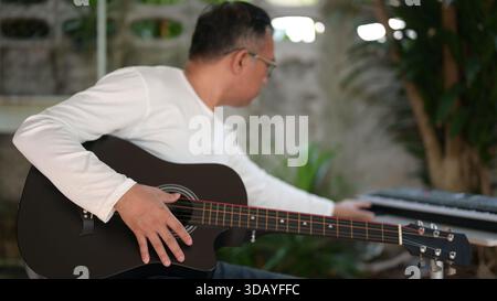 Homme dans la chemise blanche Strums guitare acoustique dans le jardin, clavier en arrière-plan, arrangement extérieur pour les entreprises Banque D'Images