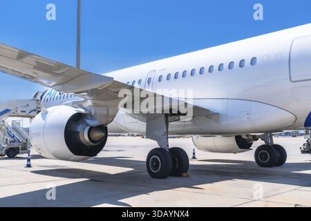 Avion de passagers stationné sur la piste de l'aéroport, présentant son aile, son moteur et son train d'atterrissage, sous un ciel bleu clair, prêt pour son prochain vol Banque D'Images