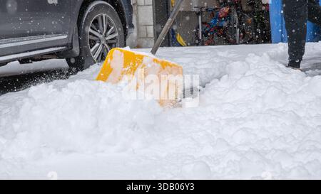 La scène de tempête de neige présente une pelle jaune vif utilisée pour déneiger une allée épaisse, soulignant le temps hivernal et l'effort extérieur Banque D'Images