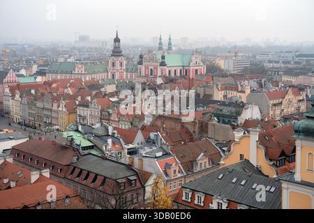 Large panorama de la vieille ville de Poznań montrant des bâtiments cathédrales, des toits rouges denses, des façades pastel, des blocs modernes lointains adoucis par la brume. Banque D'Images