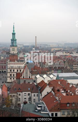Vue panoramique sur la vieille ville de Poznań montrant la tour de l'hôtel de ville, les toits rouges denses, les bâtiments pastel, les blocs de fond modernes sous la lumière grise plate. Banque D'Images