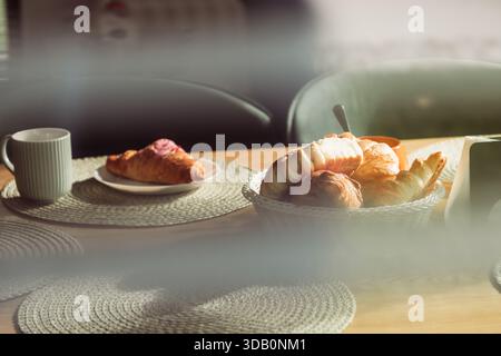 Une scène matinale confortable avec un panier de croissants et pâtisseries assorties, une assiette avec un croissant, et une tasse sur un napperon tissé. Idéal pour le breakf Banque D'Images