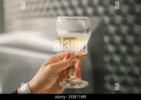 Gros plan de la main tenant un verre à vin blanc. Établissement vinicole avec cuves en acier inoxydable et lumières industrielles. Atmosphère raffinée et élégante. Banque D'Images