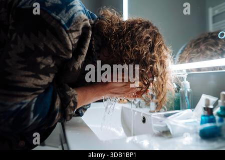 Backstage acteur laver le visage à l'évier, miroir de courtoisie éclairé et cosmétiques dispersés sur le comptoir, cheveux bouclés attachés en arrière, doux || modèle libéré Banque D'Images