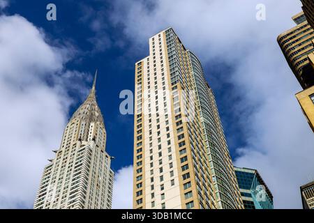 Les grands bâtiments de Manhattan s'élèvent au-dessus de la rue avec des nuages à New York City sont brillants à la lumière brillante sur leurs surfaces. Banque D'Images