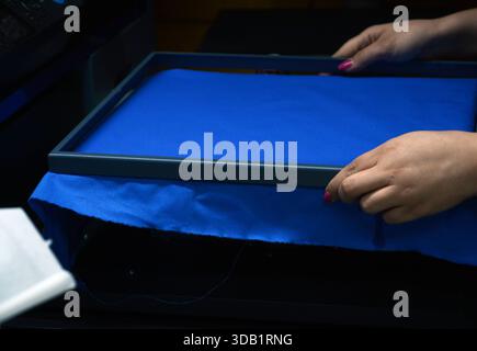 préparer la toile bleue pour l'impression avec le cadre en métal lourd dans la machine d'impression numérique et les mains de travailleuse de femme le font très habile Banque D'Images