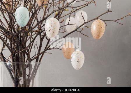 Décoration printanière de Pâques, branches naturelles et œufs pastel suspendus disposés dans un vase en verre. Décoration intérieure des vacances de printemps avec espace copie. Gros plan Banque D'Images