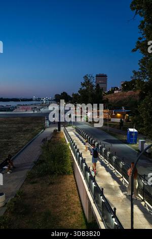 Une passerelle piétonne éclairée le long du Danube à Ruse, Bulgarie, pendant l'heure bleue, avec des gens se promenant, lumières de la ville, et un riv urbain calme Banque D'Images