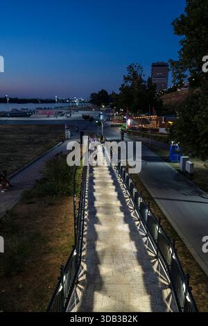 Une passerelle piétonne éclairée le long du Danube à Ruse, Bulgarie, pendant l'heure bleue, avec des gens se promenant, lumières de la ville, et un riv urbain calme Banque D'Images