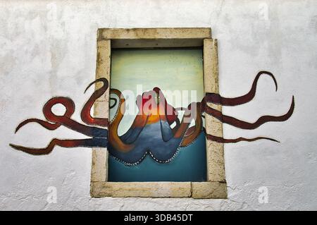 Murale colorée d'une pieuvre peinte sur un mur blanc, encadrée par une fenêtre en pierre, sur une maison à Sesimbra, Portugal Banque D'Images
