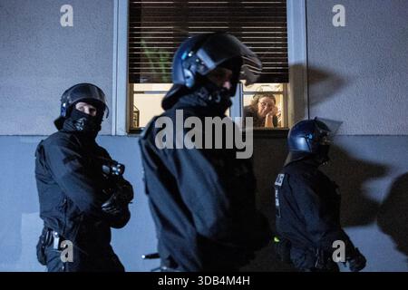 Berlin, Allemagne. 13 décembre 2025. Une femme regarde une manifestation depuis l'entrée de son immeuble résidentiel alors que des policiers passent devant le quartier et sécurisent la zone lors d'une manifestation organisée par des groupes de gauche dans le quartier de Friedrichshain. La manifestation a eu lieu lors du rassemblement annuel contre la police à Friedrichshain à Berlin (souvent appelé Journée de l'ACAB). Les participants protestaient contre les pratiques policières et les forces de l'ordre en général, et une partie de la manifestation comprenait également des slogans et des messages pro-palestiniens. Crédit : SOPA images Limited/Alamy Live News Banque D'Images