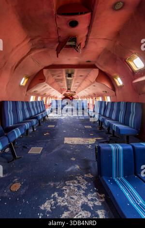 Cabine d'avion abandonnée avec sièges rayés bleus et plafond rouge écaillé - intérieur d'avion abandonné avec un long couloir symétrique et un debr dispersé Banque D'Images
