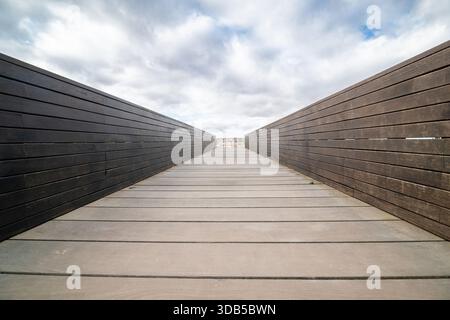 Passerelle en bois vide sous un ciel nuageux avec un mur de pierre en arrière-plan. Banque D'Images