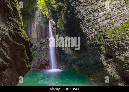 Chute d'eau en cascade plonge dans une piscine turquoise sereine dans une grotte luxuriante couverte de mousse, évoquant la tranquillité et la nature sauvage intacte de Slovenias T. Banque D'Images