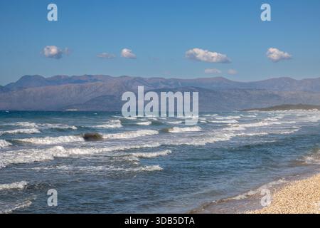 Mer Ionienne avec des vagues spectaculaires pendant une journée d'été tardive. Montagnes albanaises en arrière-plan. Ciel bleu avec des nuages blancs. Nord de l'île Corfou ( Banque D'Images