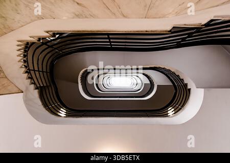 Escalier en spirale ovale regardant vers le haut - intérieur symétrique avec garde-corps noirs et ciel central Banque D'Images