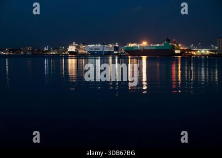 Une vue nocturne sur Southampton Water, avec un paquebot de croisière et deux porte-conteneurs amarrés aux quais. Des lumières multicolores se reflètent dans l'eau. Banque D'Images