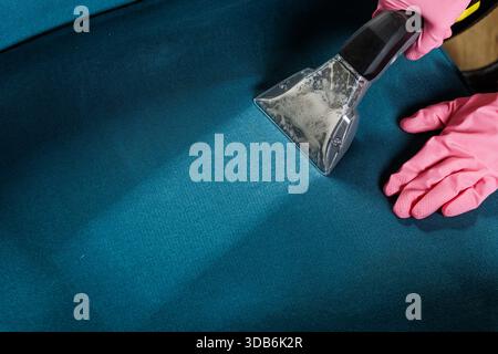 Gros plan d'un nettoyant dans des gants roses utilisant un aspirateur humide pour laver le siège du canapé, montrant le nettoyage en profondeur de la sellerie et le service de détachage. Banque D'Images