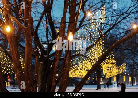 Vue rapprochée d'une ampoule chaude suspendue sur un arbre. Décoration de Noël festive avec de belles lumières bokeh dorées floues à l'heure bleue. Banque D'Images
