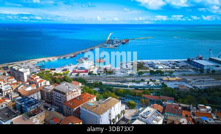 Vue aérienne large d'Ortona montrant sa mer calme, ses petites vagues du rivage, ses infrastructures portuaires, ses navires ancrés et son ciel bleu clair qui rehaussent la beauté de l'île Banque D'Images