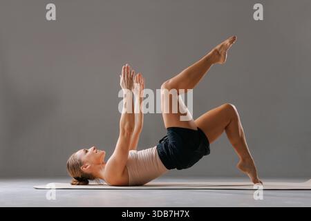 Femme en forme faisant le pont Pilates avec lifting des jambes, core et fessier entraînement sur tapis à l'intérieur. Banque D'Images
