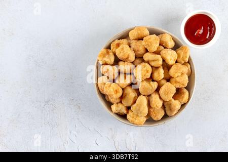 Pop-corn de poulet dans un bol avec ketchup sur fond blanc. Vue de dessus. Copier l'espace. Restauration rapide. Banque D'Images