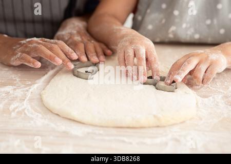 Les enfants font des cookies en faisant rouler la pâte et en utilisant des emporte-pièces dans une cuisine confortable pendant une séance de cuisson amusante Banque D'Images