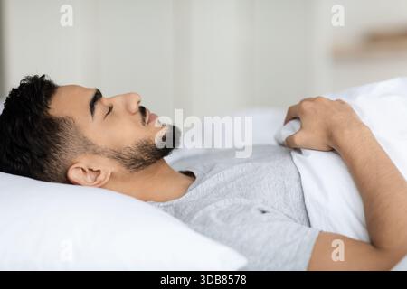 Gros plan de jeune homme arabe dormant paisiblement dans le lit à la maison pendant la journée Banque D'Images