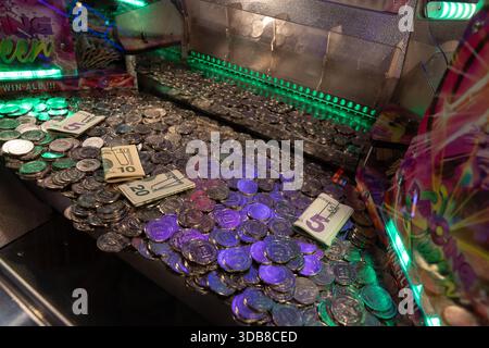 Pièces de monnaie et petits billets dans un jeu d'arcade lumineux pousseur de pièces, capturant la tension et la chance de jouer comme un casino à bord d'un bateau de croisière. Banque D'Images