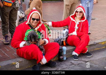 San Diego, États-Unis. 13 décembre 2025. Les participants vêtus de tenues festives s'assoient le long du trottoir avec leur chien lors d'une parade d'animaux de compagnie. Les participants et leurs animaux de compagnie ont pris part à la parade annuelle Gaslamp Quarter Pet Parade dans le centre-ville de San Diego, pendant la période des fêtes. Les chiens vêtus de costumes festifs marchent aux côtés de leurs propriétaires dans le quartier historique de Gaslamp dans le cadre d'un événement communautaire public célébrant les animaux de compagnie, la culture locale et les traditions saisonnières. Crédit : SOPA images Limited/Alamy Live News Banque D'Images