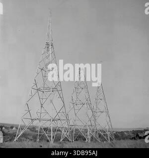 1970s. URSS. Région de Donetsk. Construction d'infrastructures pour le projet stratégique de ligne électrique de 750 kV. Une vue générale de trois mâts en acier à treillis (probablement des tours de communication radio ou une protection contre la foudre) debout dans une rangée dans la steppe. De minuscules silhouettes de grimpeurs et d'installateurs sont visibles en travaillant haut sur les structures métalliques. Un documentaire historique illustrant la complexité technologique et l'ampleur des travaux d'ingénierie dans le Donbass pacifique à l'époque soviétique. Banque D'Images