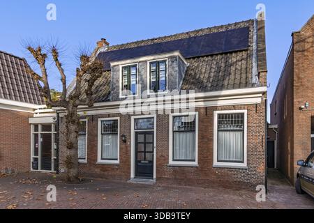 Vue extérieure d'une maison hollandaise historique avec façade en briques rouges et un toit en tuiles foncées équipé de panneaux solaires, démontrant la durabilité urbaine. Banque D'Images
