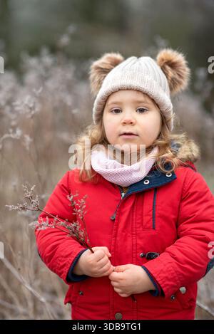 Enfant tenant de l'herbe sèche et debout à l'extérieur, face à l'appareil photo. Banque D'Images