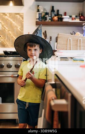 Garçon jouant au sorcier dans la cuisine tenant la baguette magique Banque D'Images