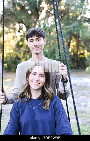 Jeune couple souriant pose étroitement sur une balançoire de corde extérieure. Banque D'Images
