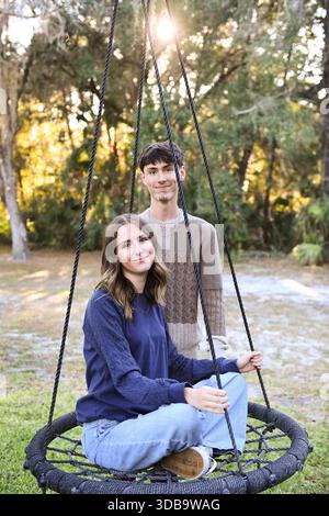 Jeune couple avec femme assise sur balançoire dans un cadre boisé. Banque D'Images