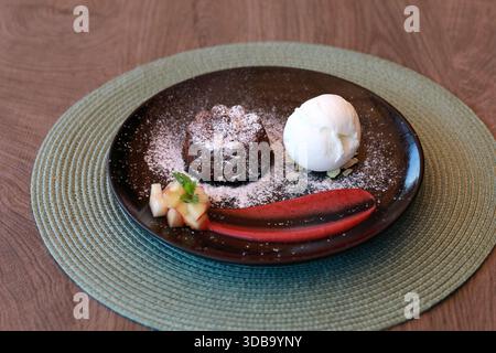 Dessert gâteau de lave au chocolat avec une boule de glace à la vanille et garniture de fruits, servi sur une assiette noire avec sauce rouge. Photographie culinaire pour le menu. Banque D'Images