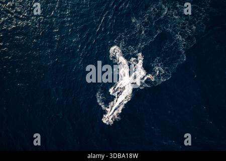 Vue aérienne d'un jet ski laissant une piste de mousse blanche sur les eaux bleu foncé de la mer, Lloret de Mar, Catalogne, Espagne. Banque D'Images