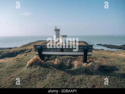 Banc en bois vide donnant sur le phare d'Elie Ness sur la côte du Fife, en Écosse, avec une mer calme et un ciel bleu clair créant un paysage côtier paisible Banque D'Images