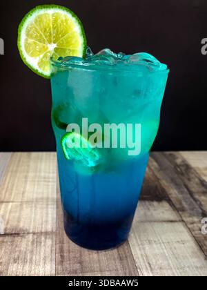 mocktail bleu lagon servi dans un grand verre avec des glaçons et des tranches de citron vert fraîches, avec un dégradé éclatant de bleu à turquoise Banque D'Images