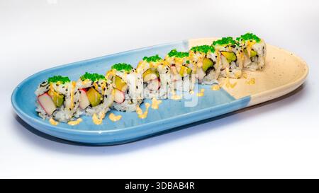 Rouleaux de sushi Uramaki avec avocat, bâtonnets de crabe, tobiko et sauce crémeuse servis sur plaque de céramique isolé sur fond blanc. Banque D'Images