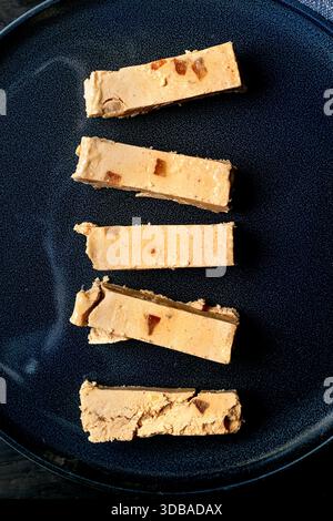 Dessert espagnol traditionnel turron orange doux classique, coupé en morceaux sur une plaque en céramique bleue. Vue de dessus, gros plan. Banque D'Images