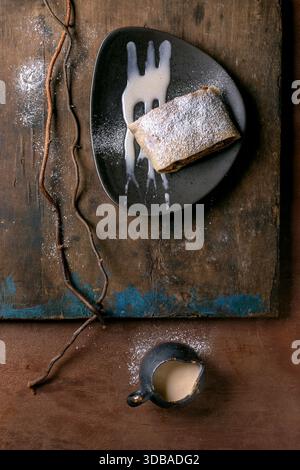 Strudel aux pommes maison traditionnel autrichien avec raisins secs. Nature morte moderne avec struddel de tranche sur plaque en céramique avec sucre en poudre et sauce. Banque D'Images
