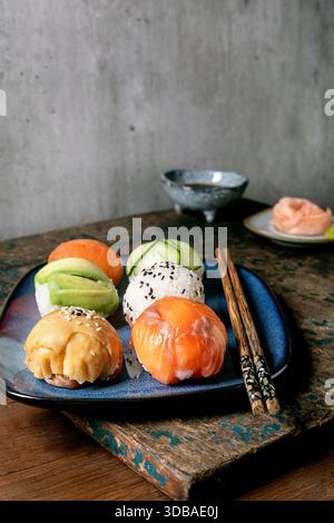 Temari sushi. Boules de sushi tendance avec saumon, avocat, concombre et omelette japonaise sur assiette bleue. Sauce soja, gingembre mariné, baguettes sur WO rustique Banque D'Images